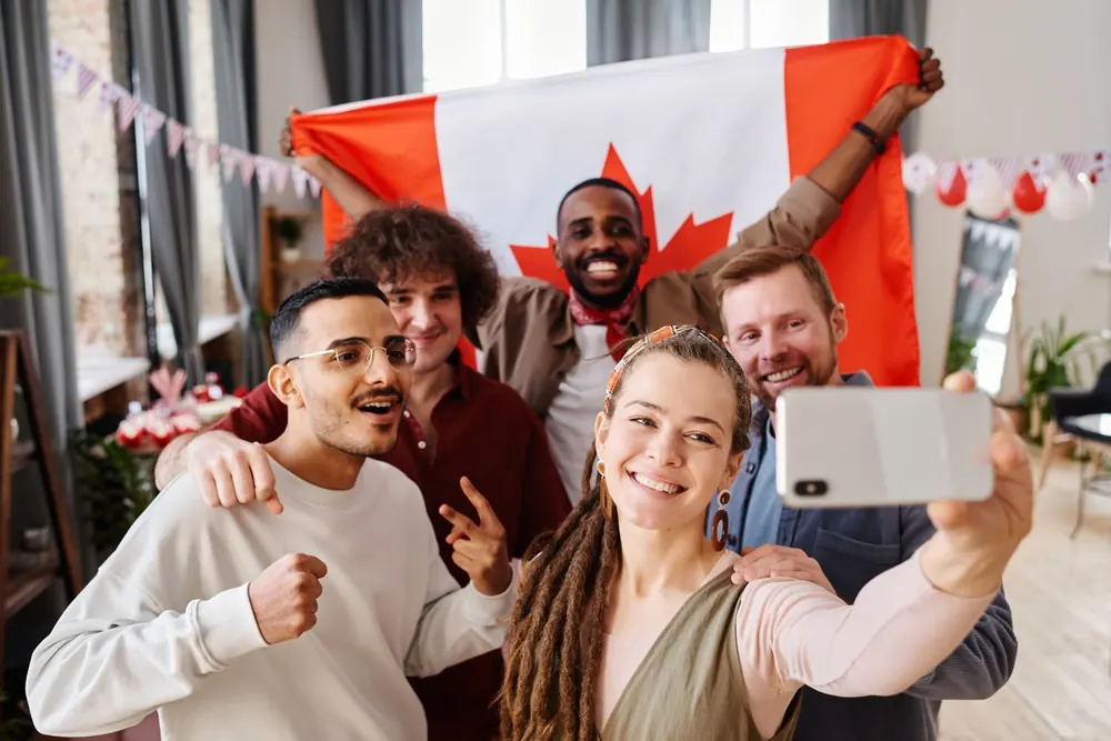 A happy group taking a selfie while a Black man holds up the Canadian flag